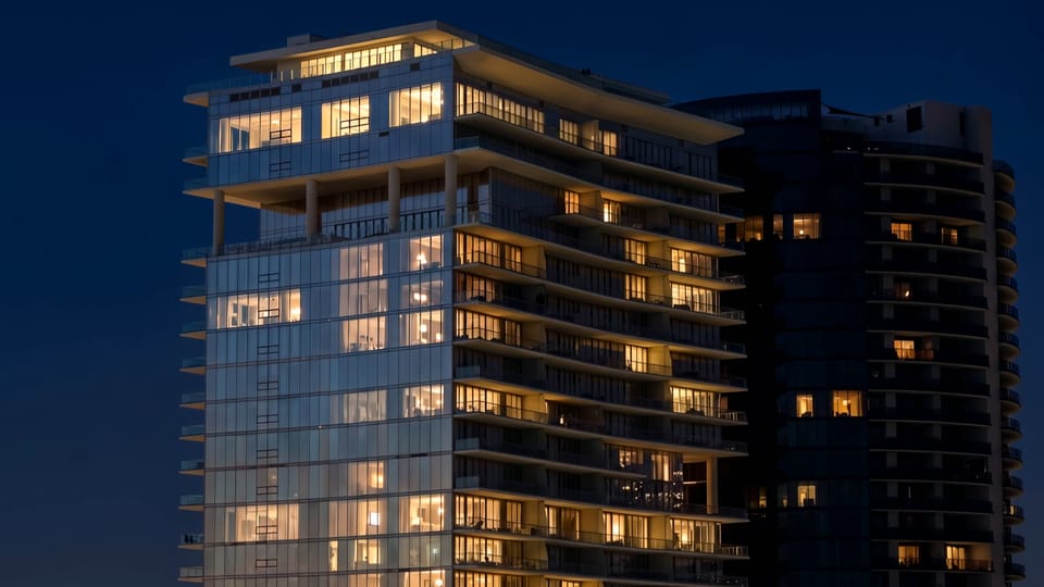 A glass apartment tower at night, most of its windows lit